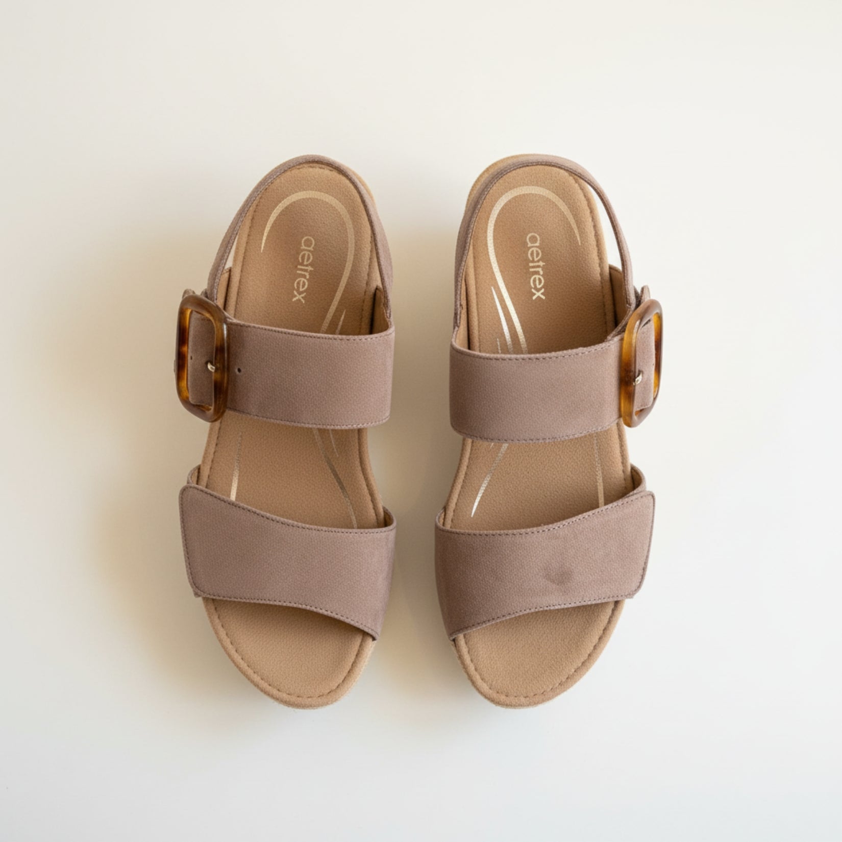Pair of taupe sandals with brown buckles on a light background