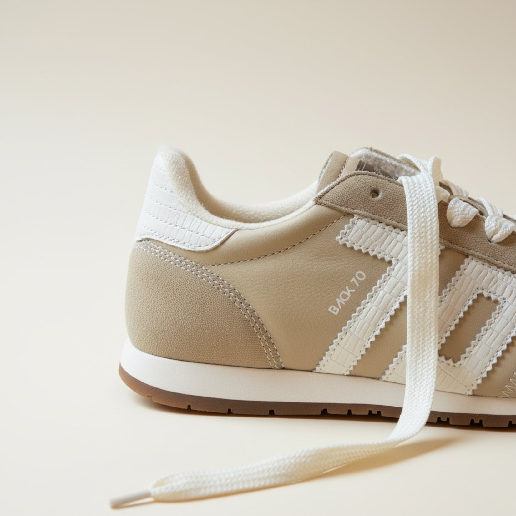 Beige sneaker with white laces on a light beige background