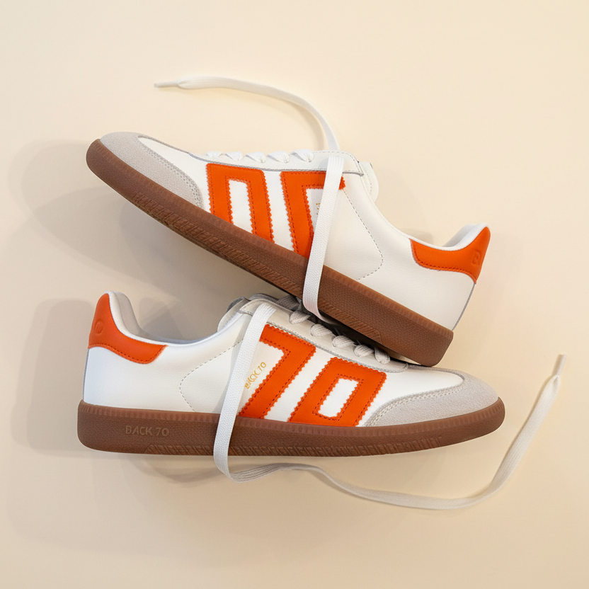 Pair of white sneakers with orange accents and brown soles on a beige background