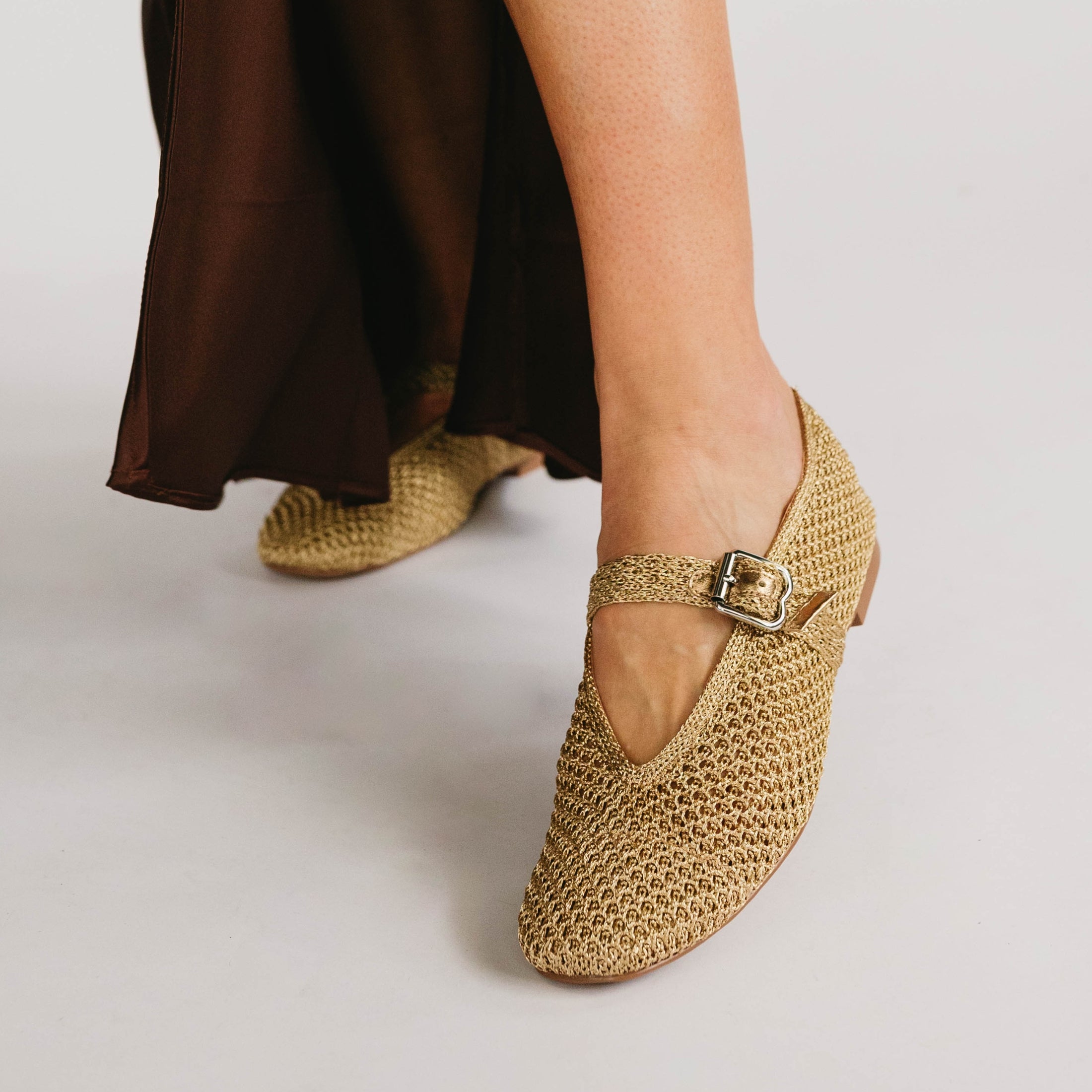 Woven gold shoes with a buckle on a neutral background