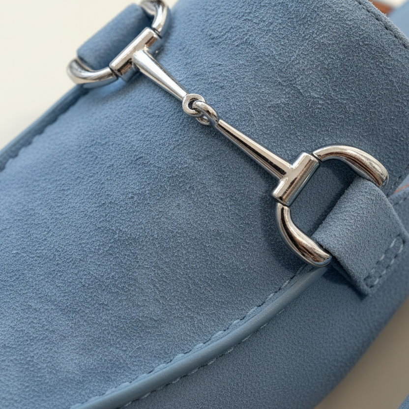 Close-up of a blue shoe with a metallic buckle detail on a beige background