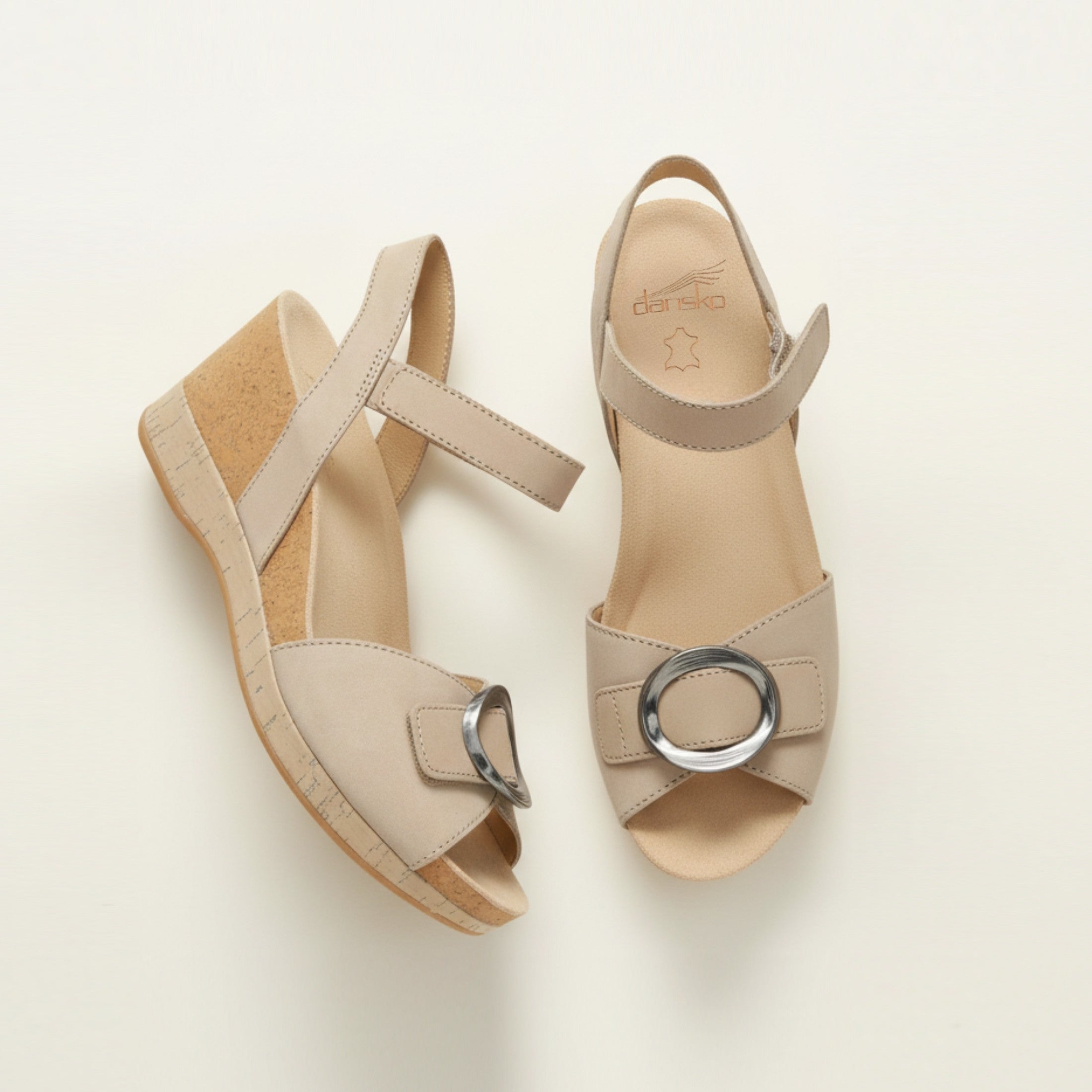 Pair of beige sandals with a circular buckle on a light background