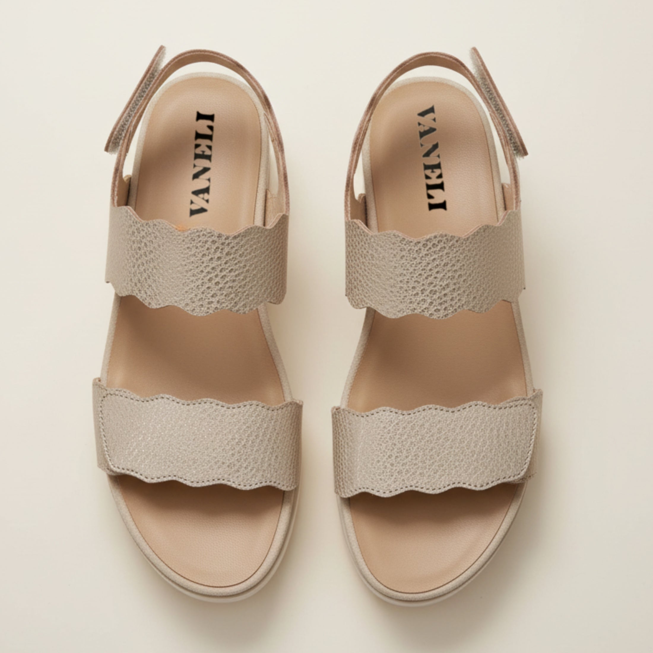 Pair of beige sandals with scalloped edges on a light background