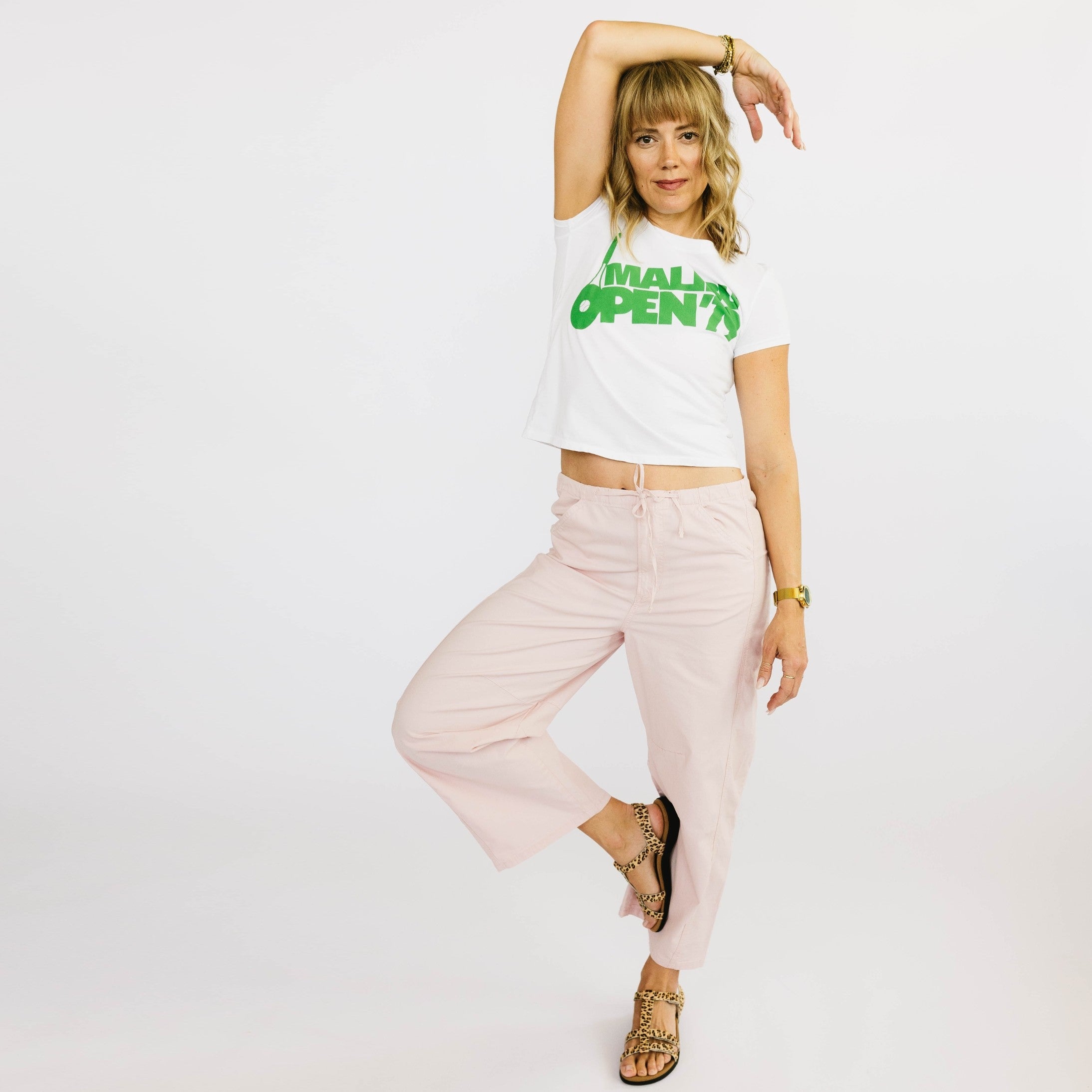 Woman wearing a white t-shirt with green text and light pink pants on a plain background