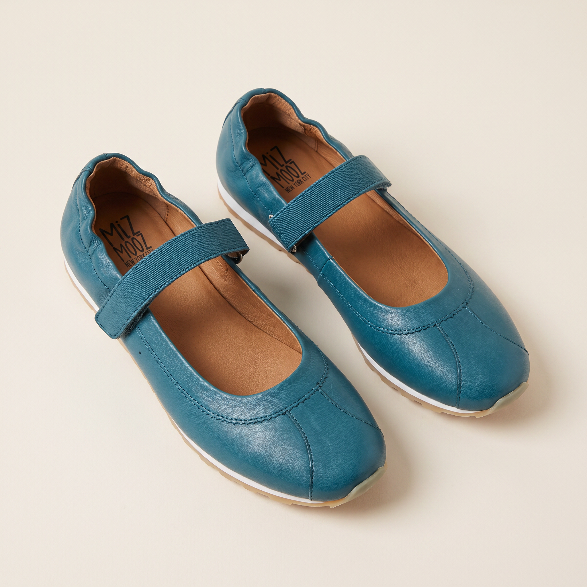 A pair of teal blue Mary Jane style shoes with hook-and-loop straps, shown on a light beige background. The brand name 'MIZ PIZZY' is visible on the insole.
