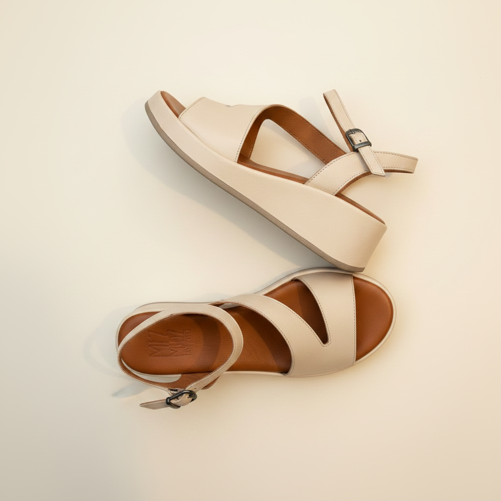 Pair of beige sandals with brown soles on a light beige background