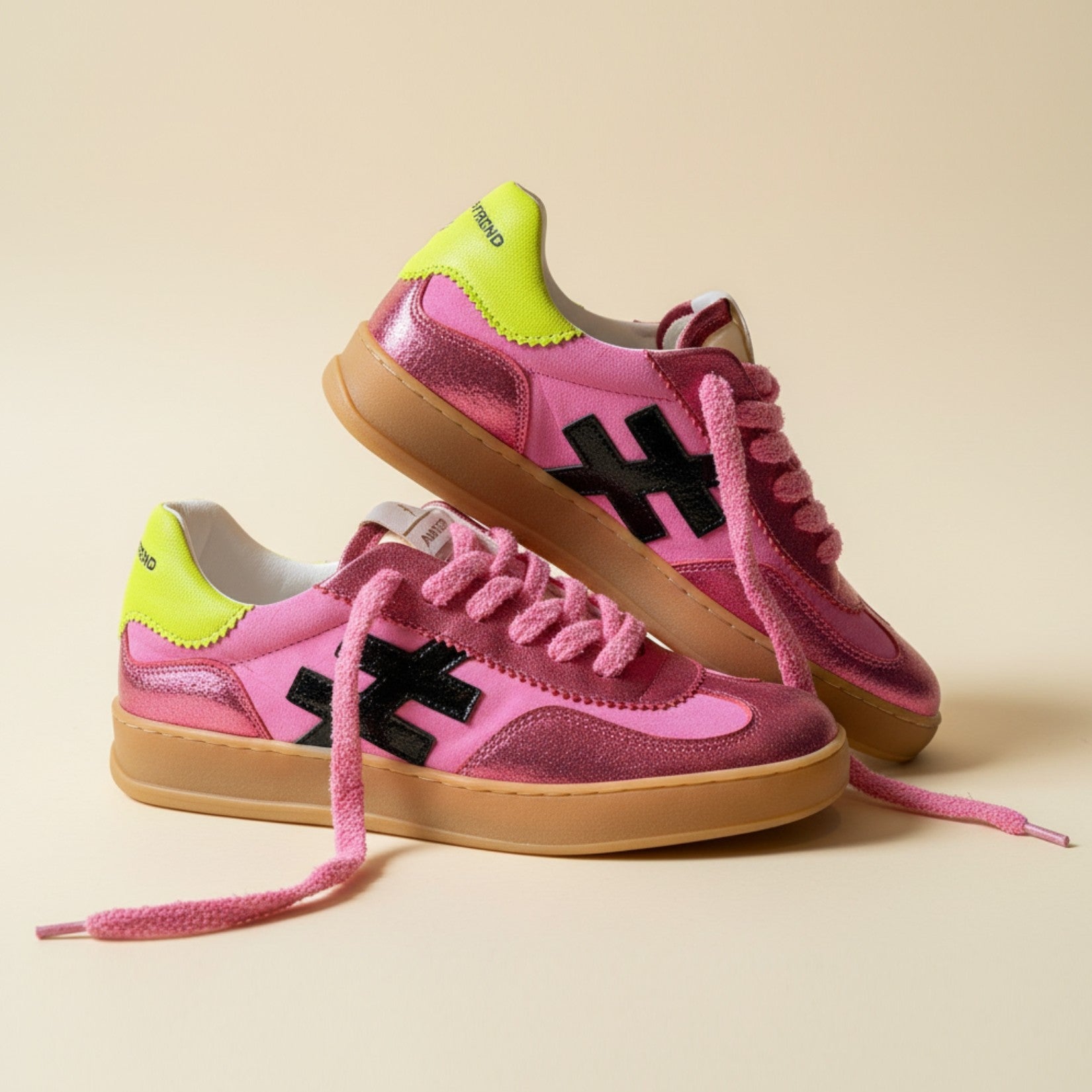 Pink sneakers with black X logo and green accents on a beige background