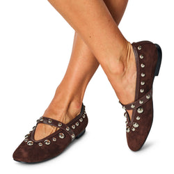 Brown suede flats with silver studs worn by a person on a white background
