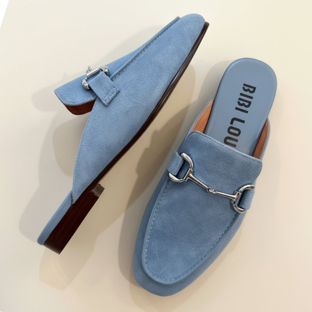 Pair of blue suede shoes with a metallic buckle on a beige background