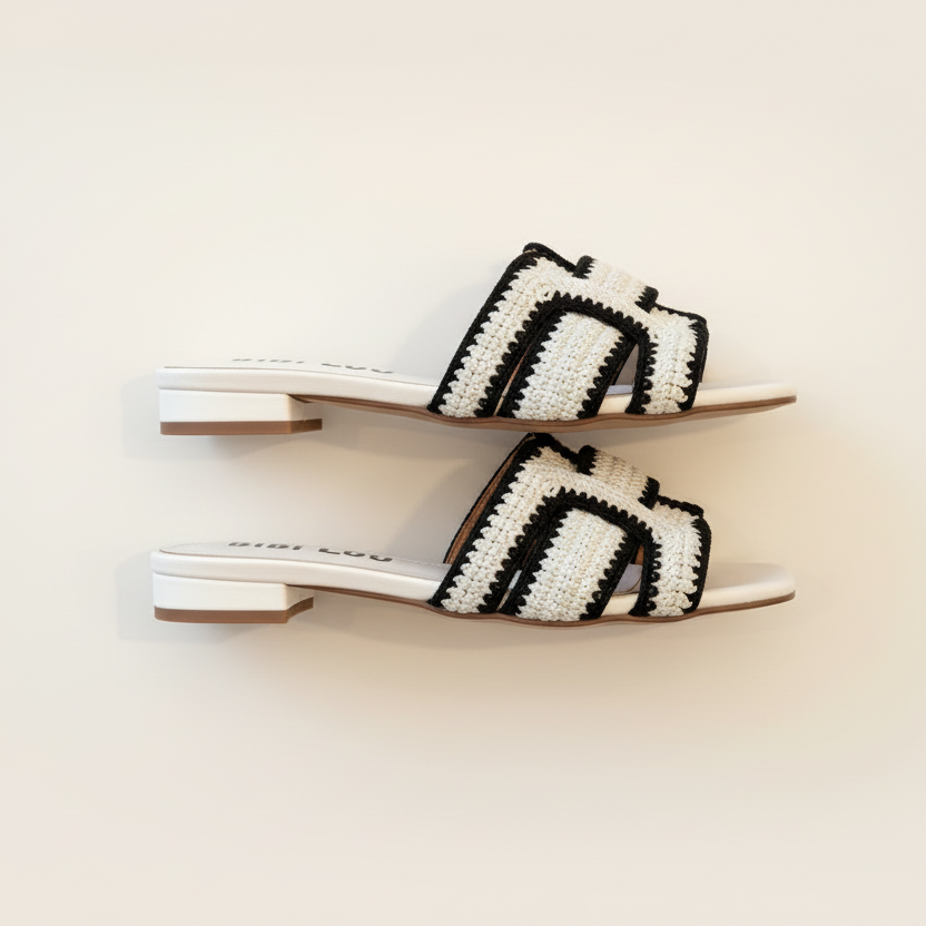 Pair of white sandals with black and white striped straps on a light beige background