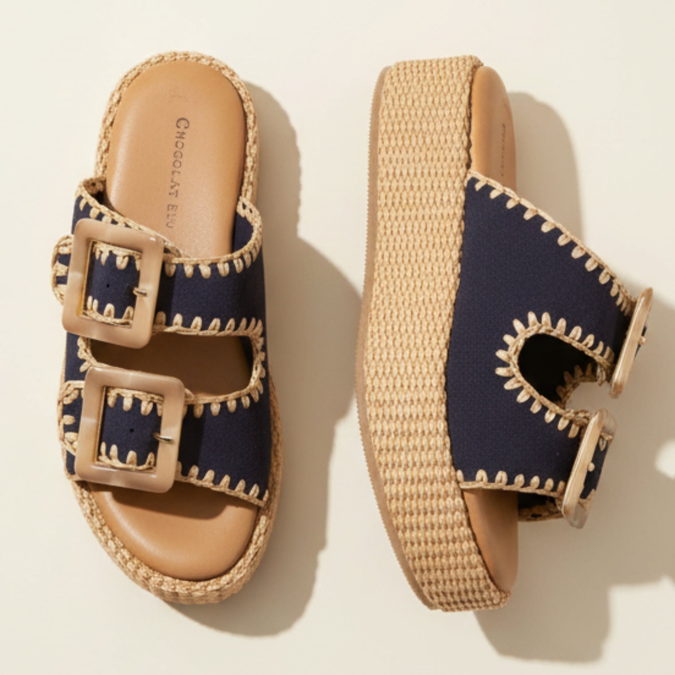 Navy sandals with brown buckles and wicker sole on a beige background