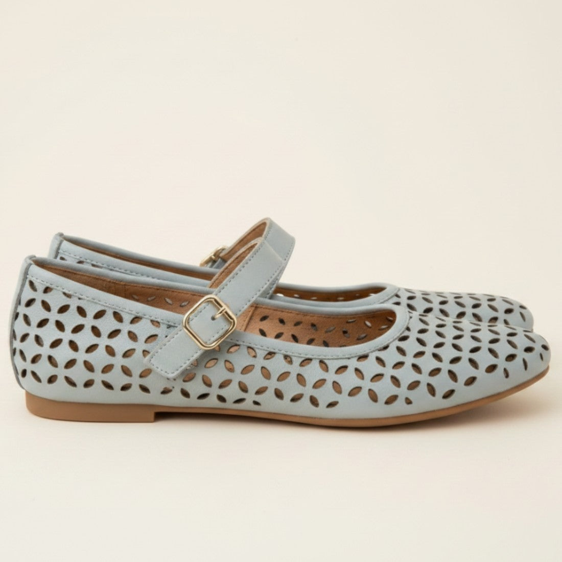 Light blue shoe with cut-out design and gold buckle on a beige background