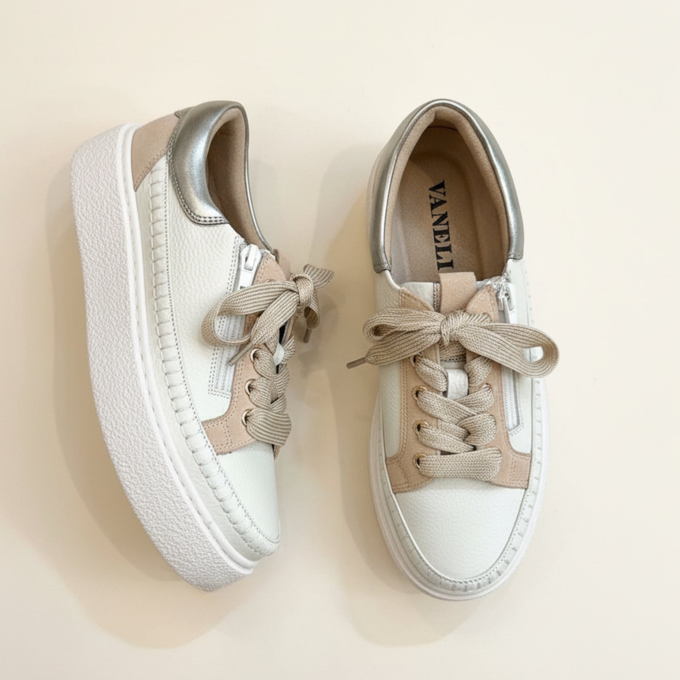 Pair of white sneakers with beige laces on a beige background
